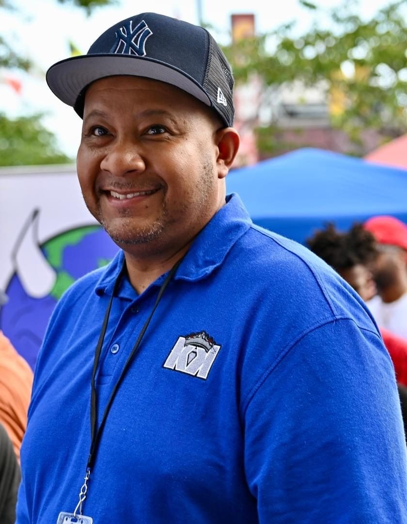 A man in blue shirt and hat smiling for the camera.