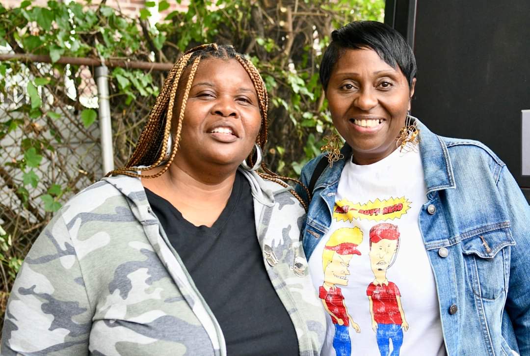 Two women standing next to each other in front of a tree.