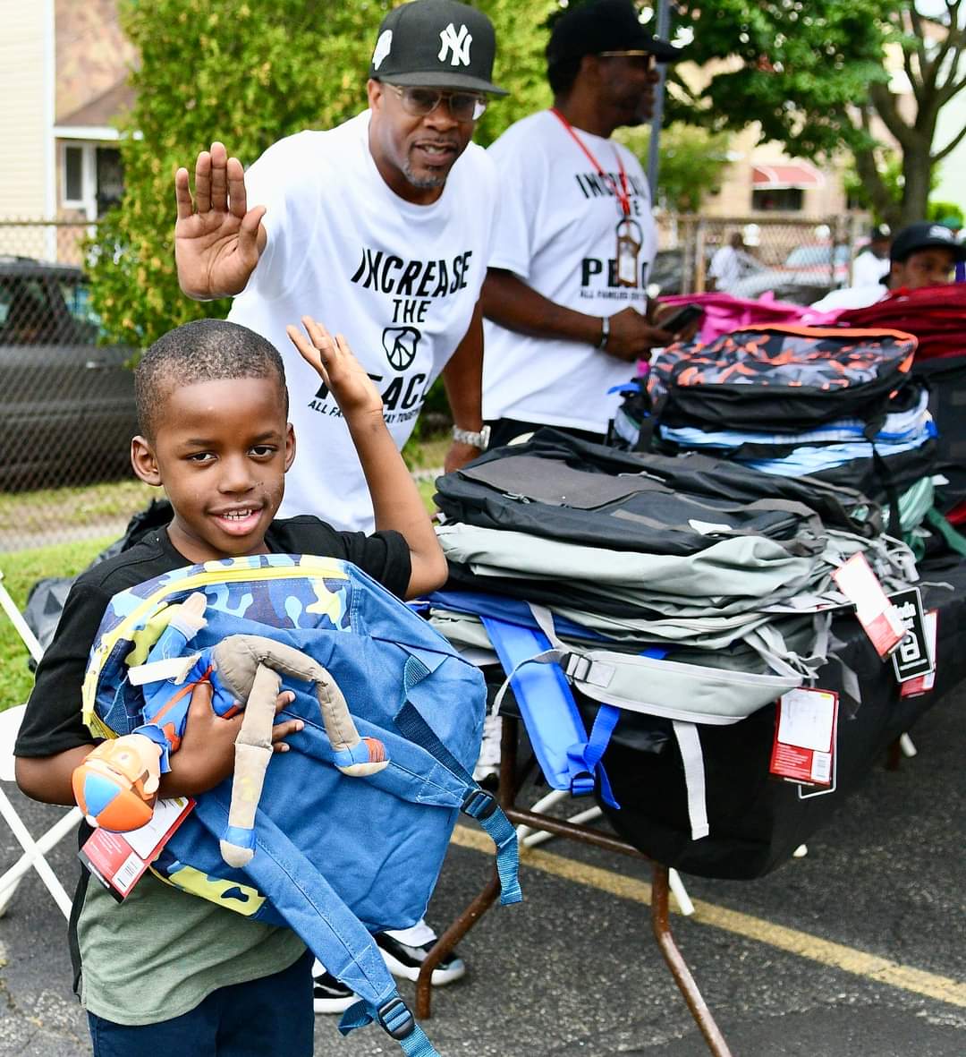 A boy holding up his backpack near some bags.